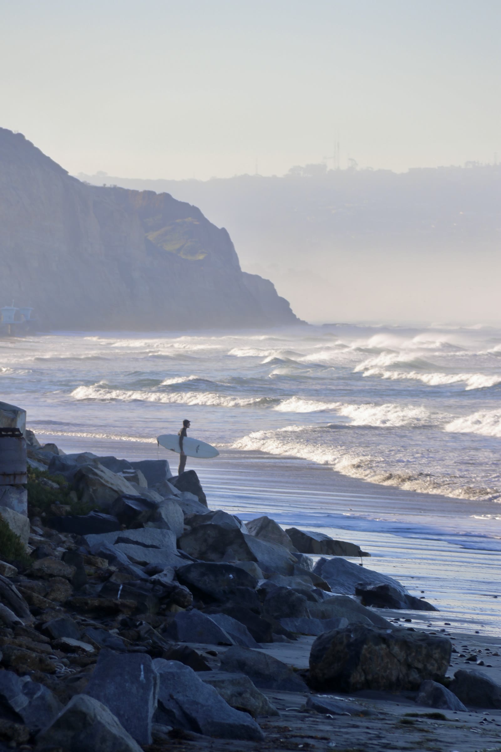 A lone surfer on the rocks below the San Diego cliffs at first light